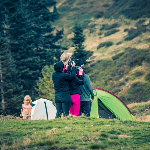 Une famille du club observe la montagne aux jumelles, près des tentes